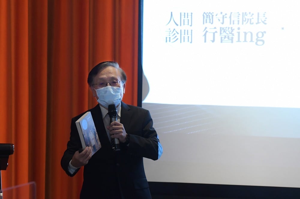可能是 1 人、站立和顯示的文字是「人間 簡守信院長 診間 行醫ing 」的圖像
