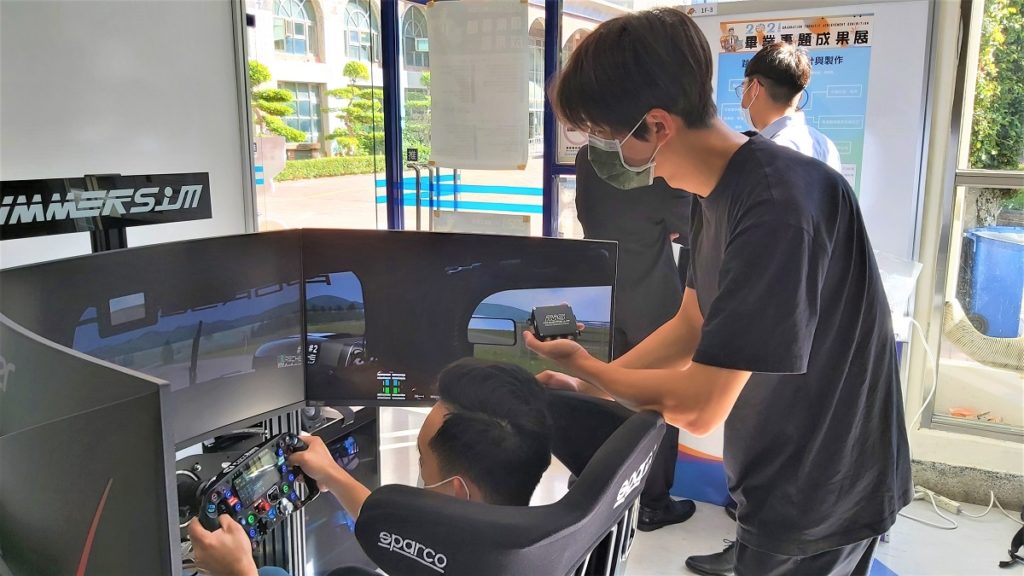 展覽現場由詹承儒實際操作賽車模擬實況,詹曜均手拿自己設計開發的專用踏板控制盒。(圖/陳惠玲攝影)