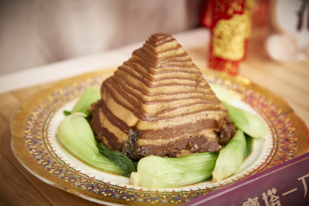 阿一鮑魚年菜「蘇杭寶塔一刀肉」,顧名思義是得一刀不斷將整塊豬五花肉,沿著邊切成薄薄的一長條肉片,阿一鮑魚附上金字塔模具,消費者加熱後,將盤子蓋上,倒扣即是完美的金字塔造型,是一道外型吸睛的御膳料理。(圖/東森購物提供)