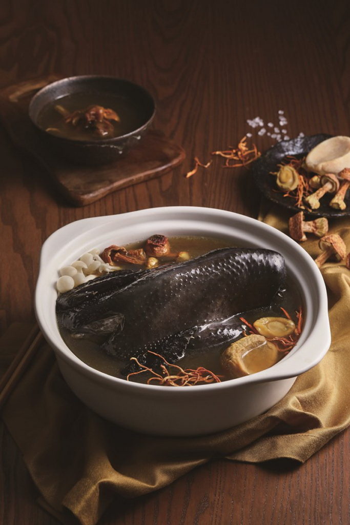 「黃金蟲草鮑魚烏骨雞煲湯」榮獲台灣百大伴手禮獎肯定,嚴選台灣烏骨雞及黃金蟲草,肉質鮮甜入口即化,湯頭醇香四溢。(圖/六福旅遊集團提供)