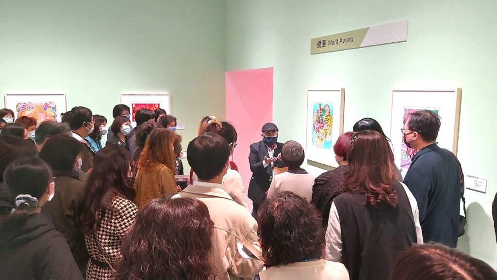 版畫評審委員鐘有輝於展覽現場為國美館志工導覽得獎作品。（圖/陳惠玲攝影）