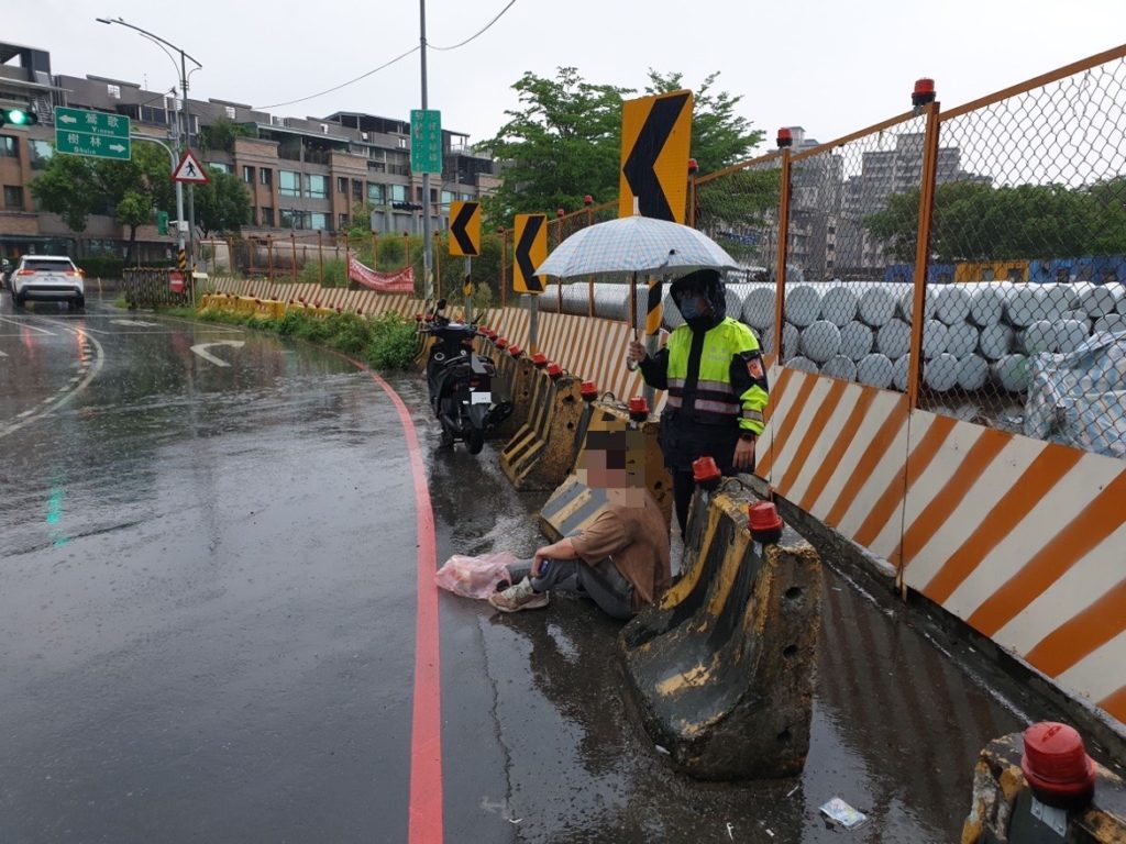 樹林分局山佳派出所警員何洹、張育齊在滂沱雨勢下，撐傘協助車禍騎士擋雨-