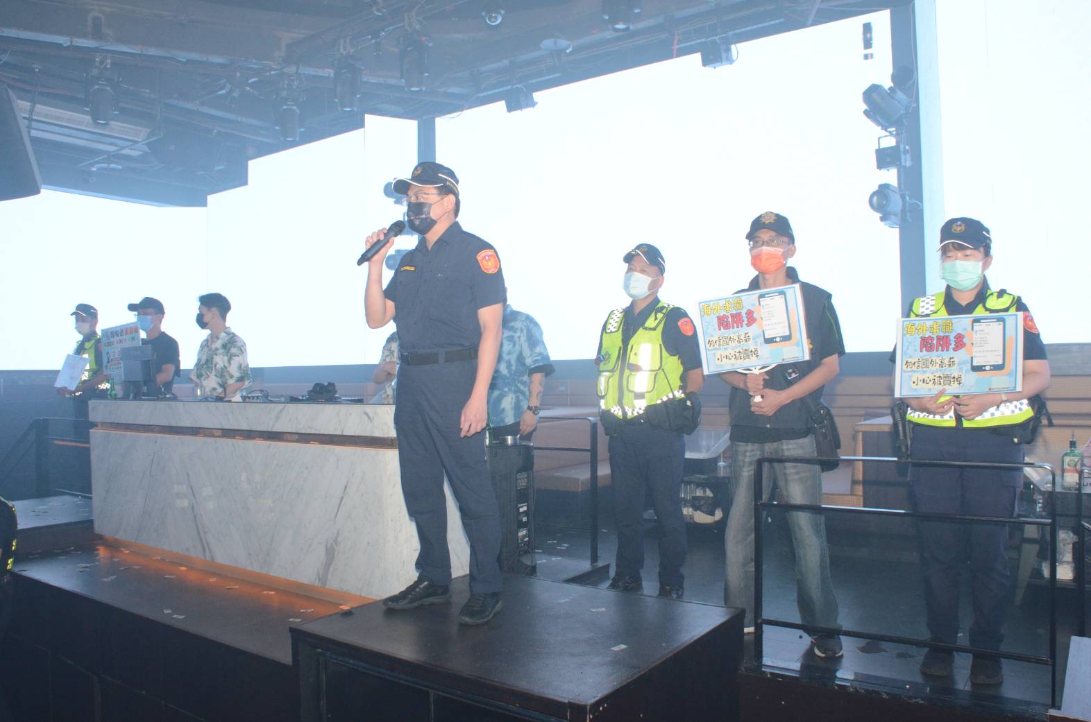 圖片說明：日前中市警六分局副分局長劉忠和於前往西屯區夜店臨檢，於DJ台上宣導搭配手持拿看板，以押韻標語「海外打工要小心，被當豬仔會痛心」讓更多年輕族群知道打工詐騙的嚴重性。(記者謝榮浤翻攝) 