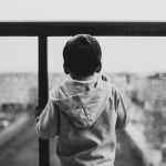 backview of sad child waiting on a glass window