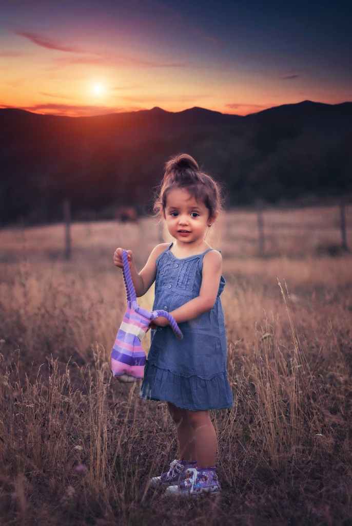 girl in blue dress standing on grass field during sunset