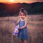 girl in blue dress standing on grass field during sunset