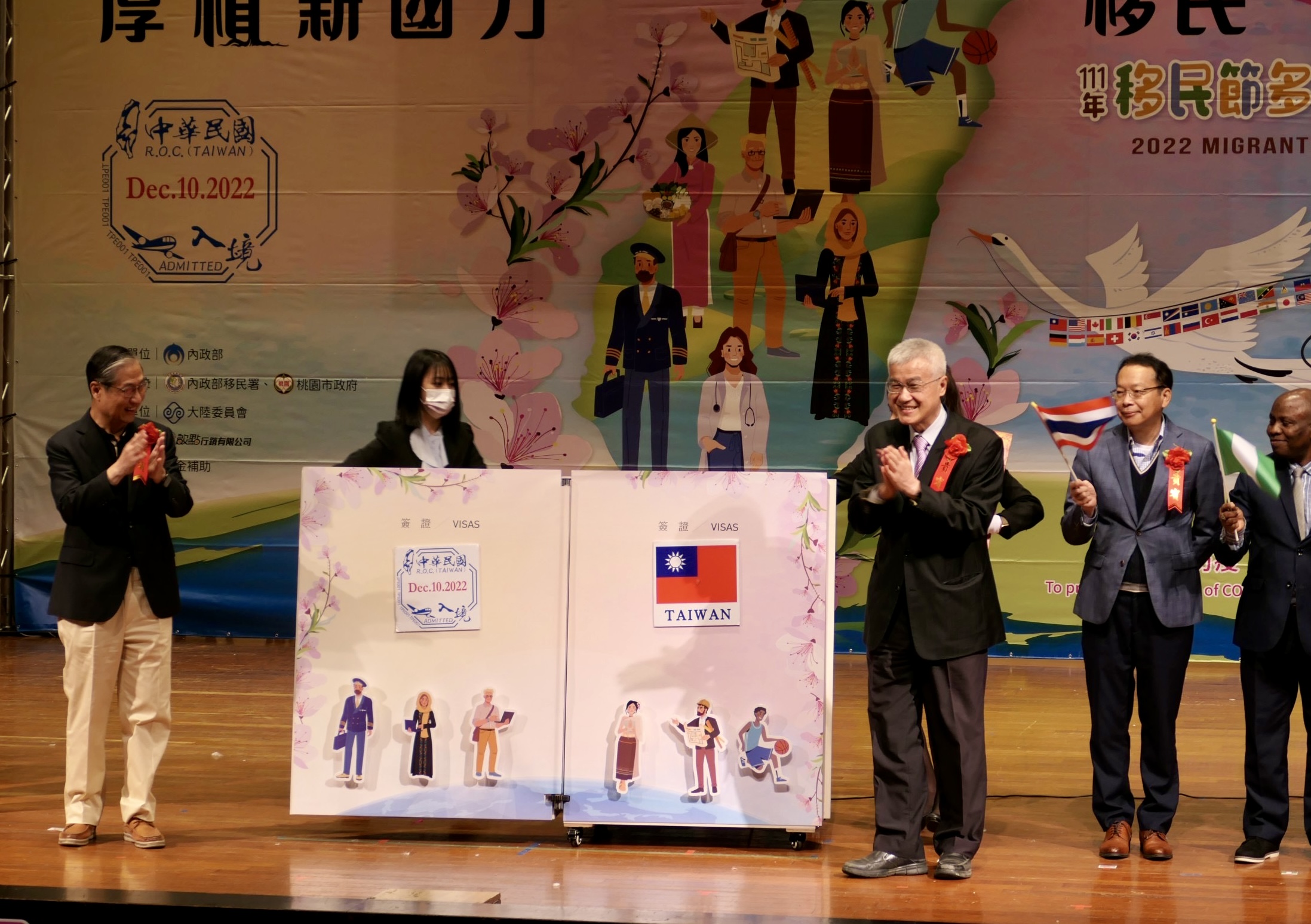 移民署署長鐘景琨(左一)與桃園市副市長李憲明(右三),分別於魔法書上蓋下象徵中華民國入境查驗章及國旗,揭開移民節活動序幕。(記者馬治薇攝)