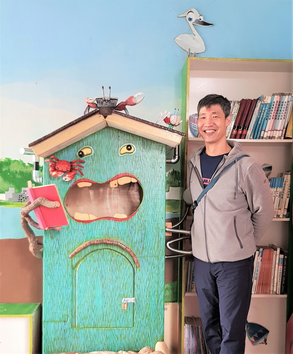 冠德玉山教育基金會將木藝家陳志宏二次創作的再生木藝裝置作品《愛吃書怪獸》贈送給歡度百年校慶的新北市米倉國小,圖為陳志宏與作品合影。(圖/冠德玉山教育基金會提供)