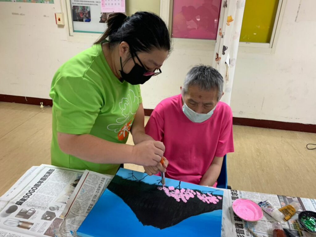 重度心智障礙者大俠(右)，為中心內最年長的長輩，在伊甸工作人員鼓勵之下，他提筆創作