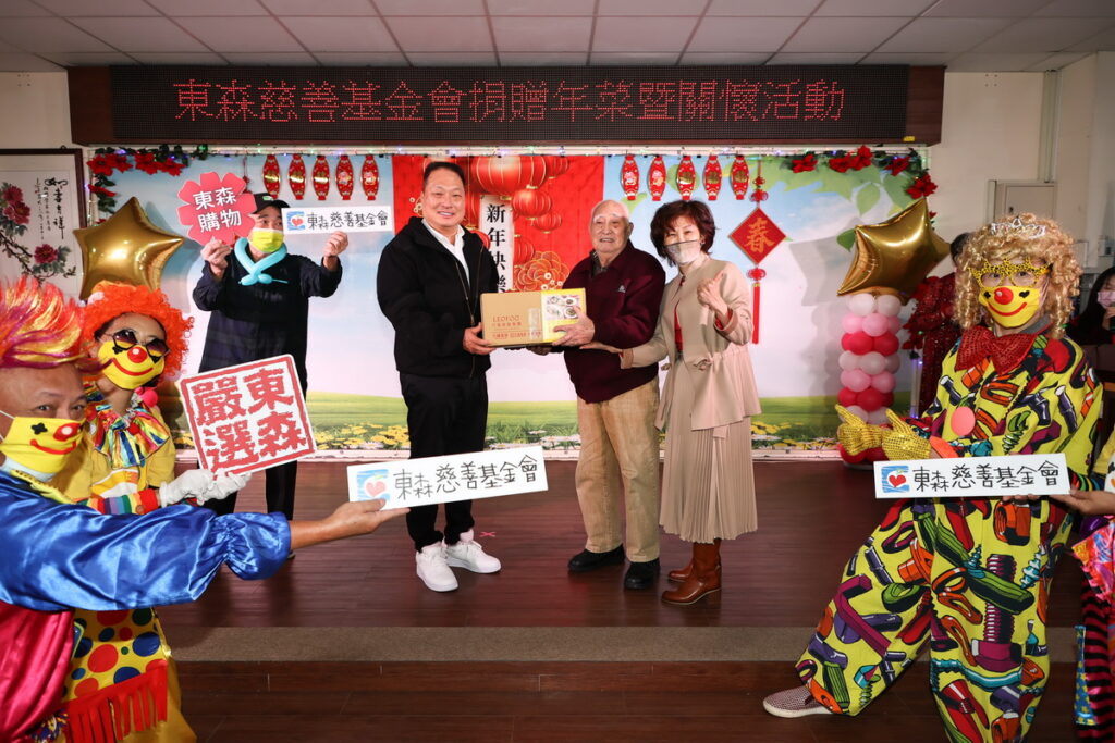 圖說: 王令麟捐贈板橋榮民之家年菜組合,由榮民之家家主任陳桂美(圖左)陪同百歲人瑞(圖中)代表受贈。