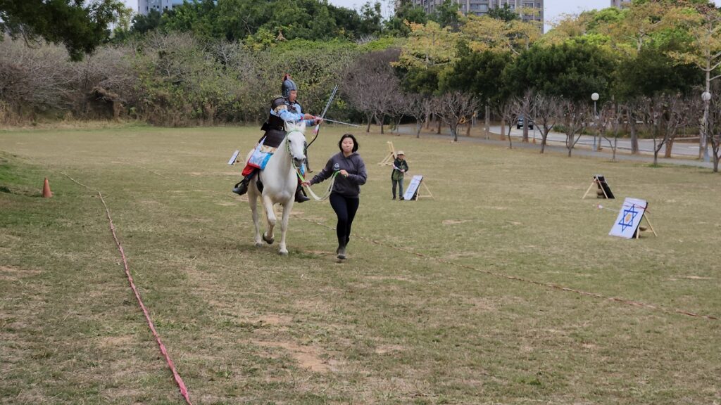 在東海湖旁大草地,台灣騎射大師鍾國華表演古裝騎兵射馬武藝,馬術社學生在旁協助。(圖/陳惠玲攝影)