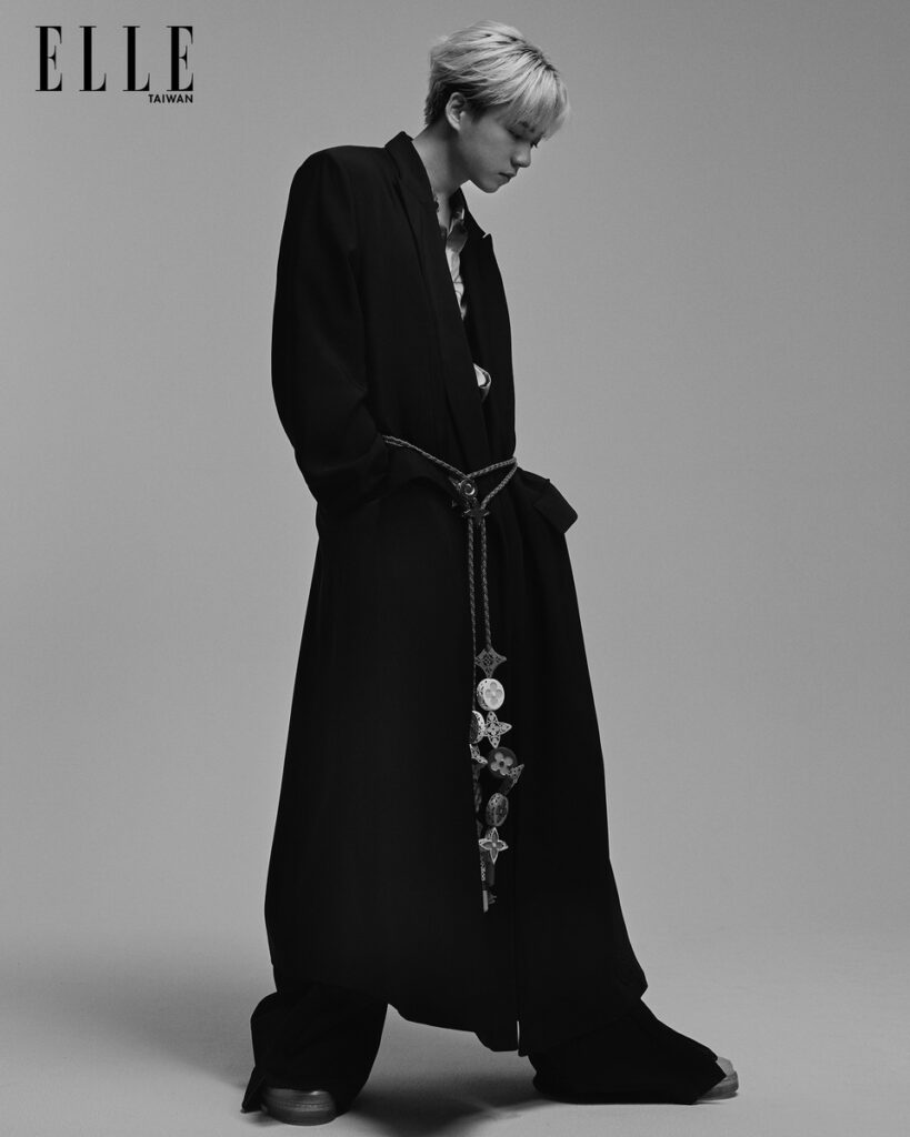 祖安,印花襯衫、黑色寬版長褲、墜飾腰帶寬版大衣、休閒鞋(ALL BY LOUIS VUITTON)。(照片轉載自「《ELLE》國際中文版雜誌」)