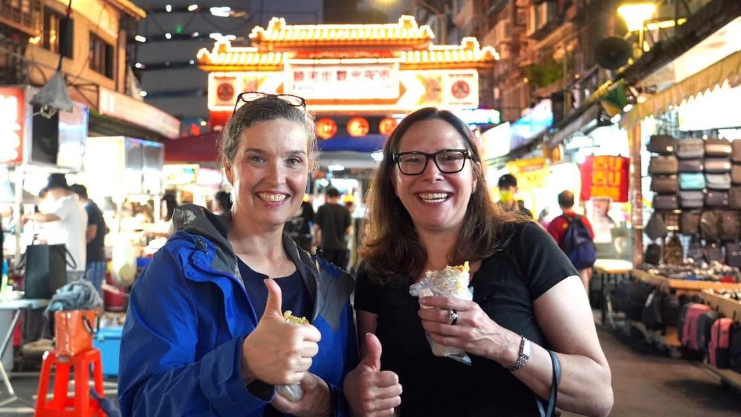 AIT處長孫曉雅(左)帶訪台的AIT主席羅森伯格(右)逛饒河夜市,兩人品嘗潤餅捲,羅森伯格大讚好吃。翻攝AIT臉書