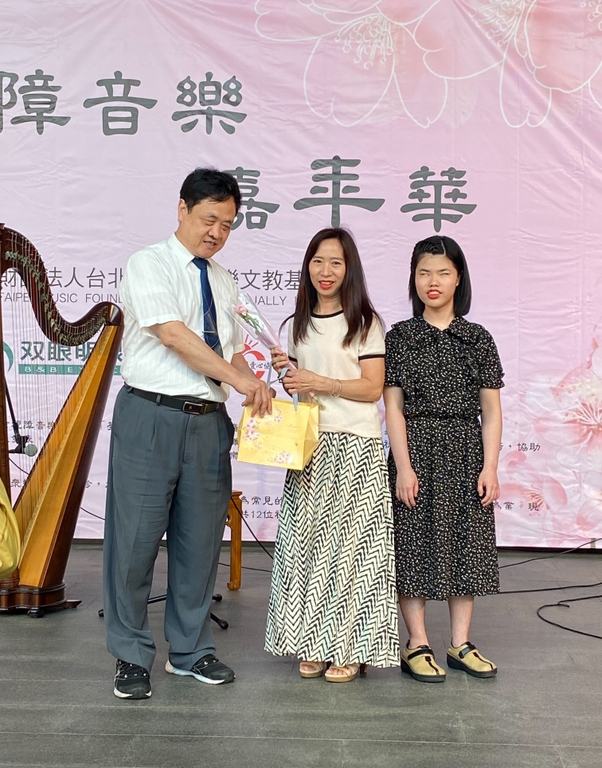 （左一）視障音樂基金會董事張育豪致贈禮品給學員母親