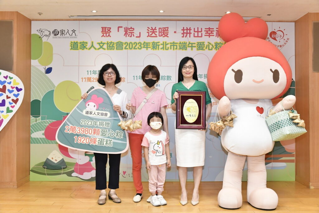 協會理事長張旖(右二)、新北市社會許秀能副局長(左一)及協會公益大使發心娃娃，與出席代表受贈的家戶合影留念