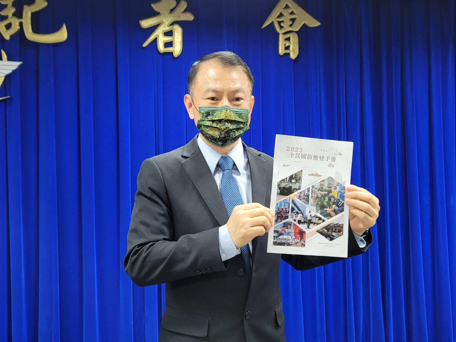 共軍已換裝21式軍服,但全民國防應變手冊卻印解放軍07式軍服,供民眾辨識;圖為全動署物力動員處處長沈威志在記者會上展示手冊的照片。資料照片/王烱華攝