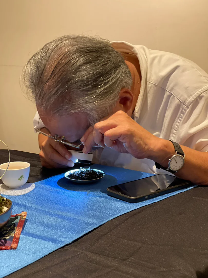 ▲汐止社大講師高松根教授用40倍放大鏡檢視超過四十年的建順茶行老茶葉。（照片 / 蘇凡媛）