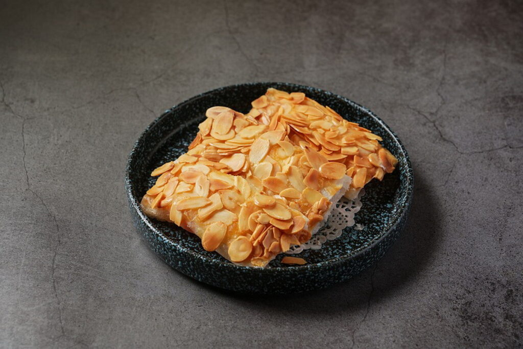 「生汁明蝦卷」整尾的澎湖明蝦川燙後,再以糖漬鳳梨丁、美乃滋攪拌均勻調味,以威化紙包裹、表層塗抹蛋黃液,再鋪上杏仁薄片入鍋油炸。(圖/神旺潮品集.忠孝店提供)