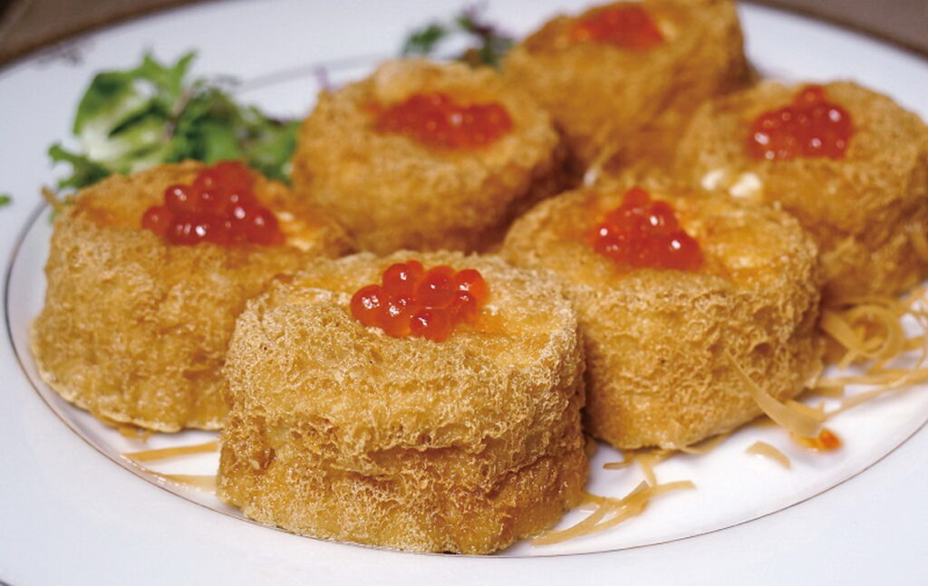 「鳳巢魚子炸豆腐」選用板豆腐中間掏空泡鹽水後油至金黃酥脆,內餡塞入以咖哩醬拌炒的雞肉丁、聖女番茄粒、蘑菇粒,佐上鮭魚卵,最後以春捲皮切絲油炸後鋪底點綴。(圖/神旺潮品集.忠孝店提供)