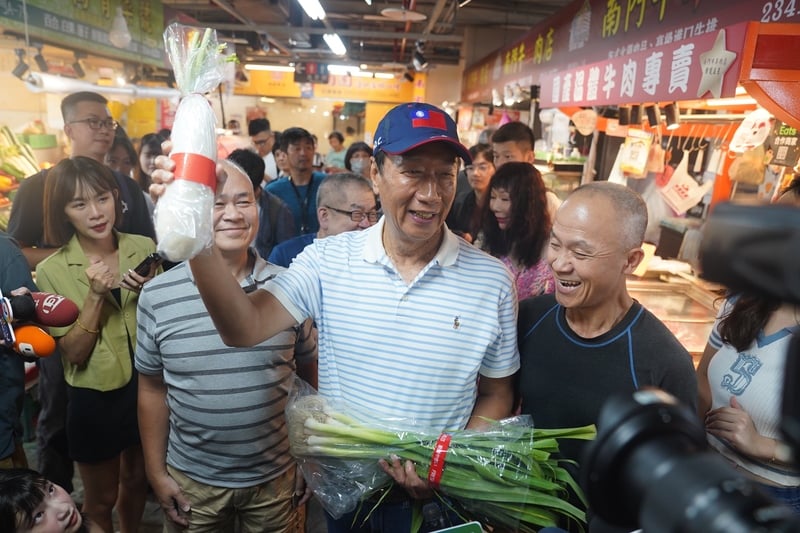 鴻海創辦人郭台銘(中)今參訪南門市場,受到攤商熱情歡迎,有人送他青蒜表達支持。中央社