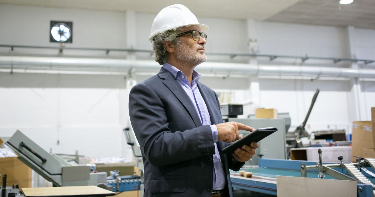 1200-serious-supervisor-white-helmet-holding-tablet-looking-manufacturing-process