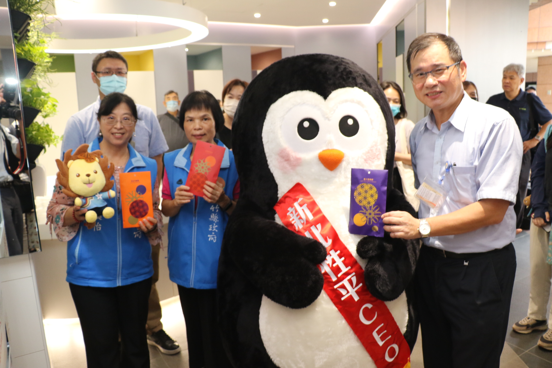 新竹縣社會處長陳欣怡(左起)、參議詹秀連帶著「性平大師(獅)」皮皮獅在新北市性平CEO企鵝暖爸的引導下從「見紅就發」生理用品發送機取出衛生棉右為新北市社會局專委林坤宗.。(圖/新北市政府提供)