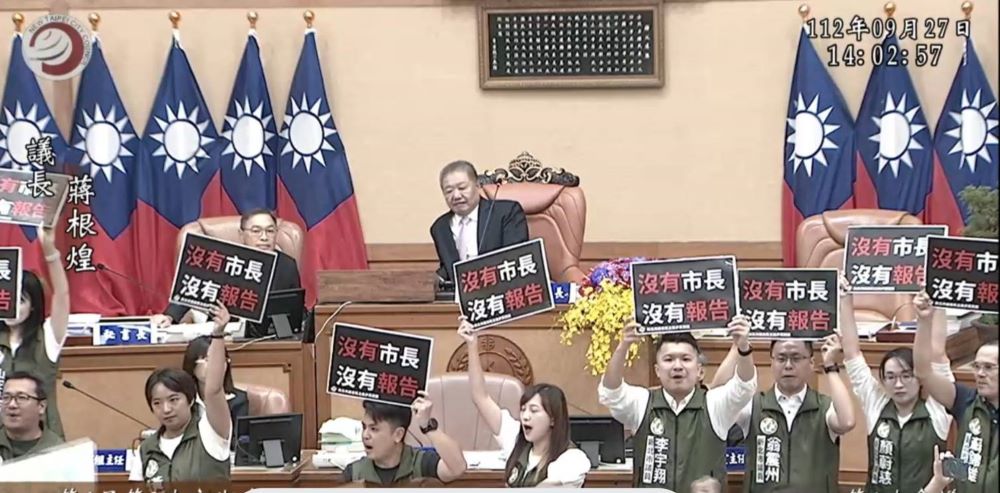 《圖說》新北市議會今日開議,民進黨議員舉牌高喊「沒有市長、沒有報告」,佔據發言台並強力阻擋代理市長、劉和然副市長上台報告。〈記者葉仁富攝自議會視頻〉