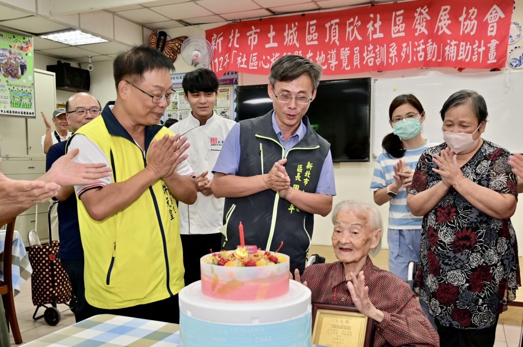 頂新里長許元皇為祝福里內龍桂英阿嬤今年滿百歲，特別在巿民活動中心準備大蛋糕慶賀。(圖/新北市政府提供))