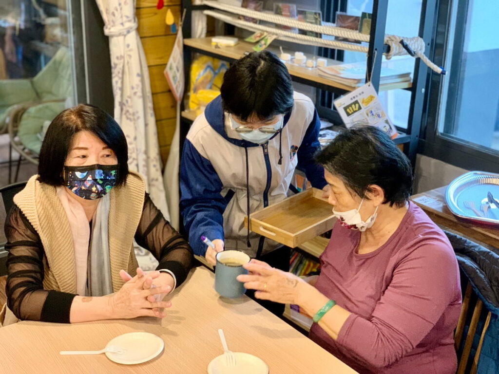 在「一日社區服務」裡,瑤瑤(中)雖然緊張,仍然很認真完成任務,端來咖啡與社區長輩分享(芥菜種會提供)