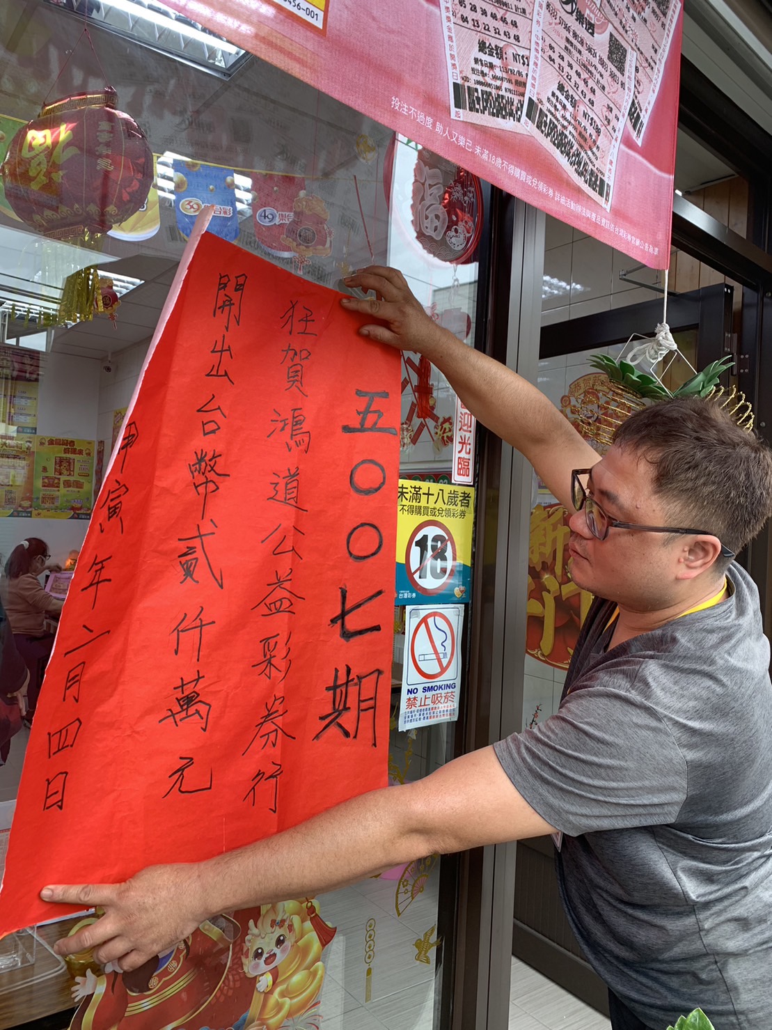 今年「2000萬超級紅包」刮刮樂第一個頭獎得主是由彰化縣花壇鄉「鴻道公益彩券行」開出，老闆黃任鋒貼紅榜分享喜氣。（記者張溎壕攝）