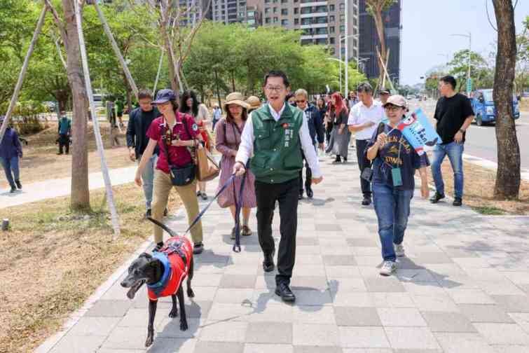 ▲ 來自20組毛孩家庭的大大小小狗狗們，一致配戴高雄市動物友善品牌「伴bàn」圖樣的三角巾，全程穿著禮貌帶（或生理褲），在家人繫繩牽引下，依序在輕軌月台等車、上車、下車。（高雄市政府提供）