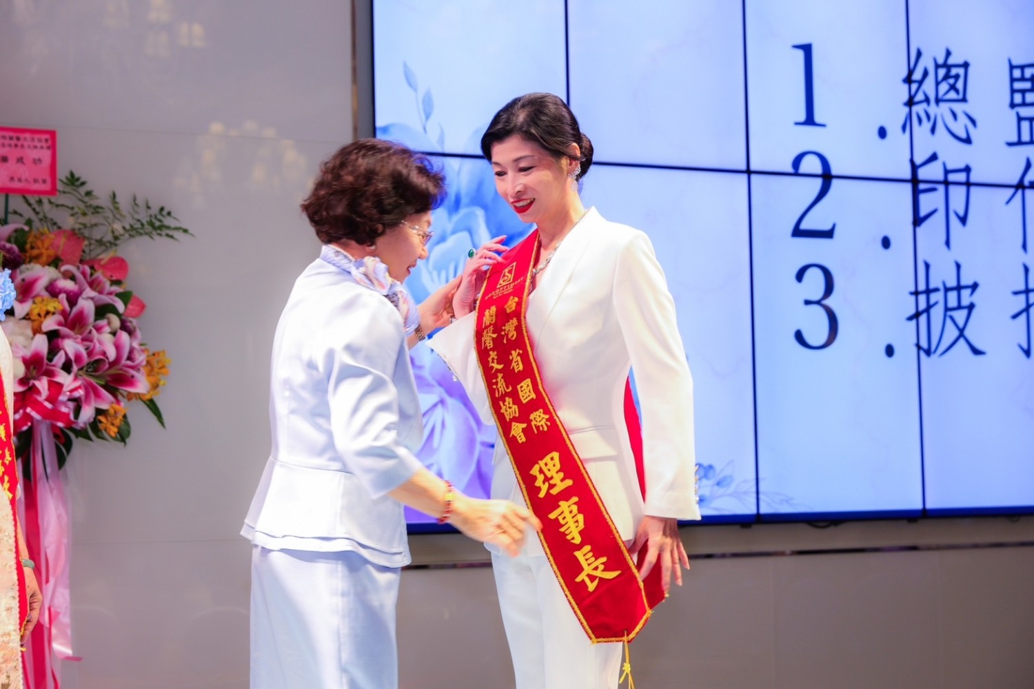 台灣省國際蘭馨交流協會創會總監蔡鈴蘭為新任理事長蔡佳欣披掛綵帶。(記者張欽翻攝)