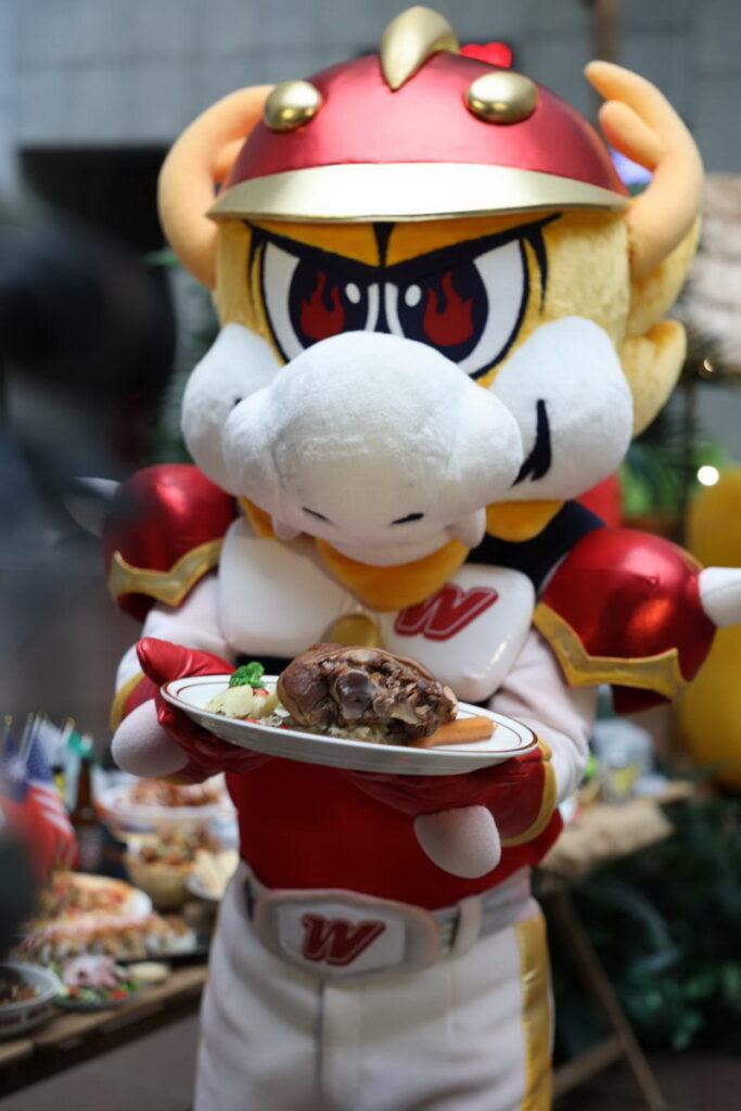 味全龍棒球隊吉祥物猛哥現身市府中庭,手持天母味特色料理邀請民眾前往天母商圈看棒