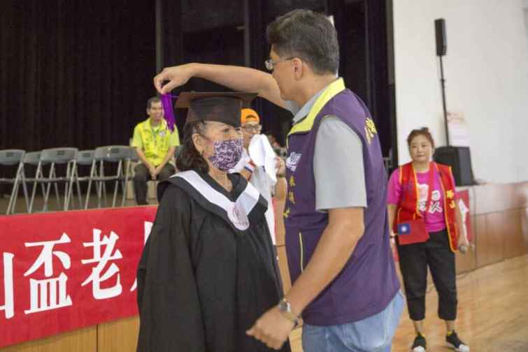 ▲華山基金會今天在大葉大學舉辦「彰化區第9屆愛老人運動會」，特別安排了一日學子體驗，讓賴阿嬤代表長者挑戰了五個關卡，象徵完成了未曾實現的學業夢想，並穿上學士服，由參議柯呈枋進行了撥穗儀式。（華山基金會提供）