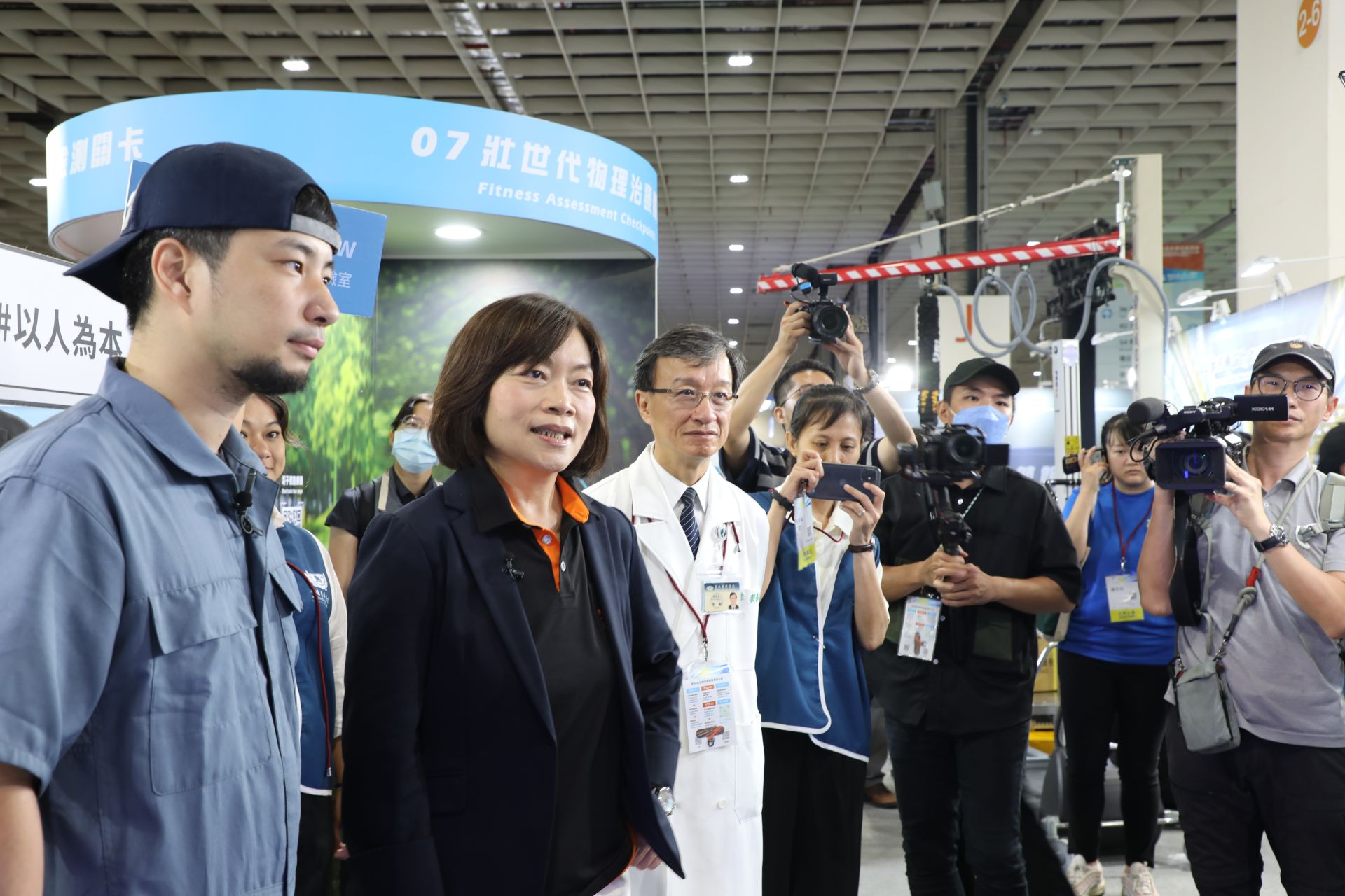 勞動部部長何佩珊(左二)在直播主超認真少年(左一)陪同下，來到「主題展示區」壯世代菁采館展，花蓮慈濟醫院「i菩提x FedGPT」展區。左三圍花蓮慈院醫務秘書李毅醫師。