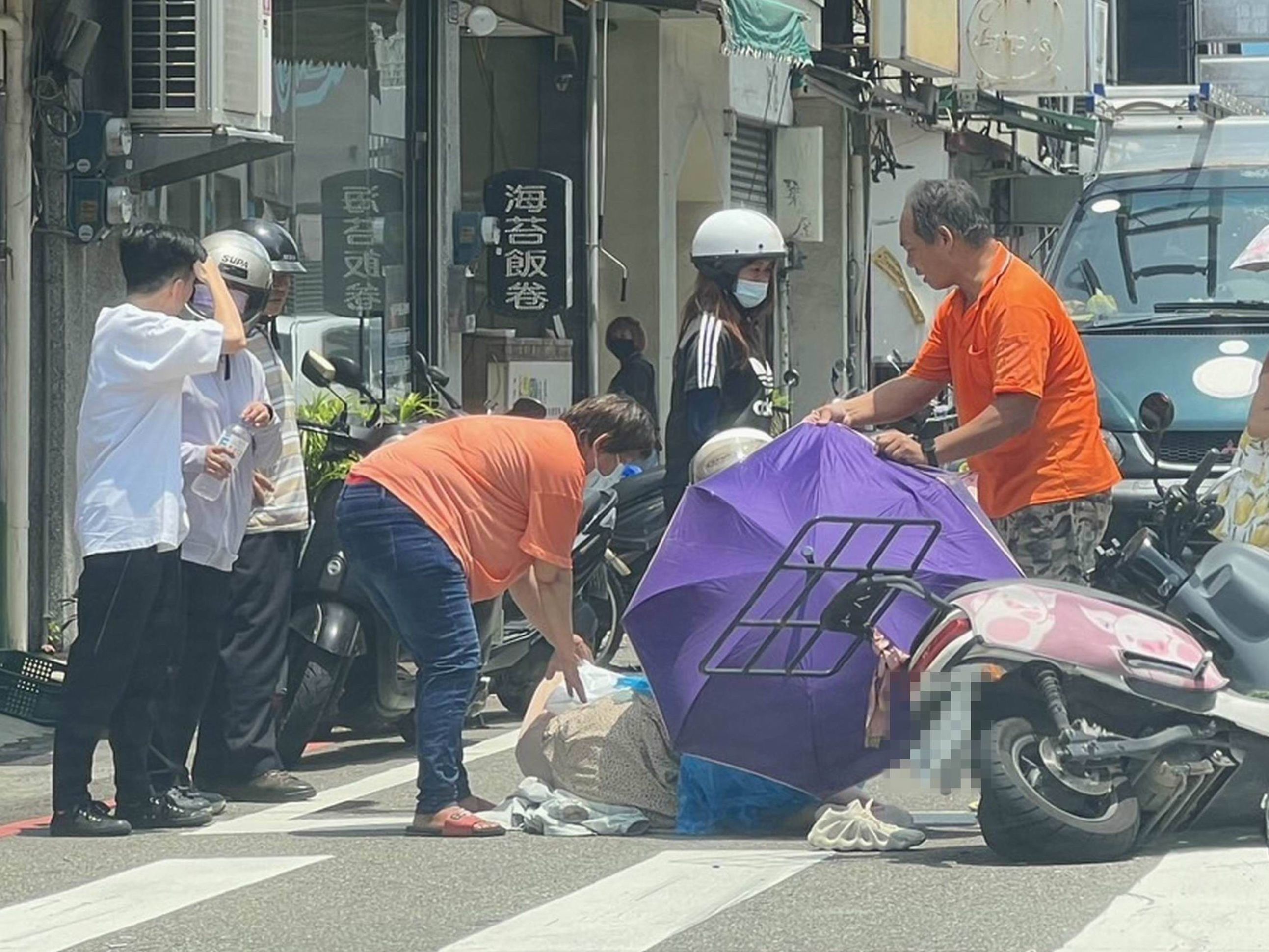 ▲彰化市發生一起機車與轎車碰撞車禍，適逢中午柏油路面滾燙，有人撐傘為倒地的女子遮陽防曬傷。（民眾提供）