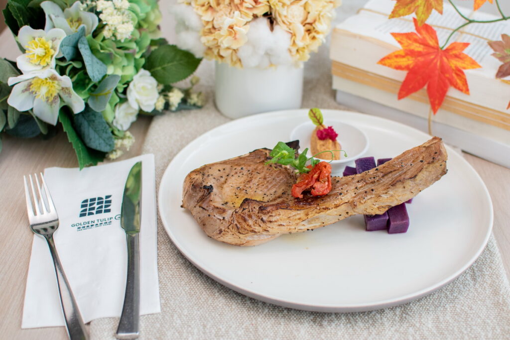 必嚐佳餚「戰斧豬佐麥寮花生沾醬」,這道料理選用了沿著豬肋骨切出的戰斧豬排,經過主廚細心地煎至完美熟度,佐以主廚特製來自麥寮的香濃花生沾醬。(圖-將捷金鬱金香酒店提供)
