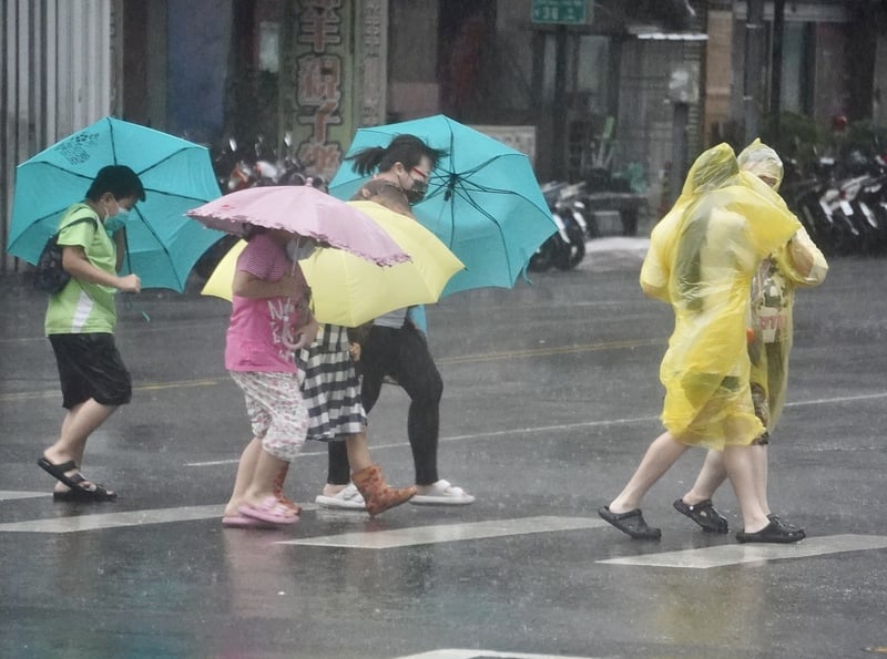 山陀兒颱風來襲,街頭民眾穿著雨衣、撐傘在強風雨勢中前行。 中央社