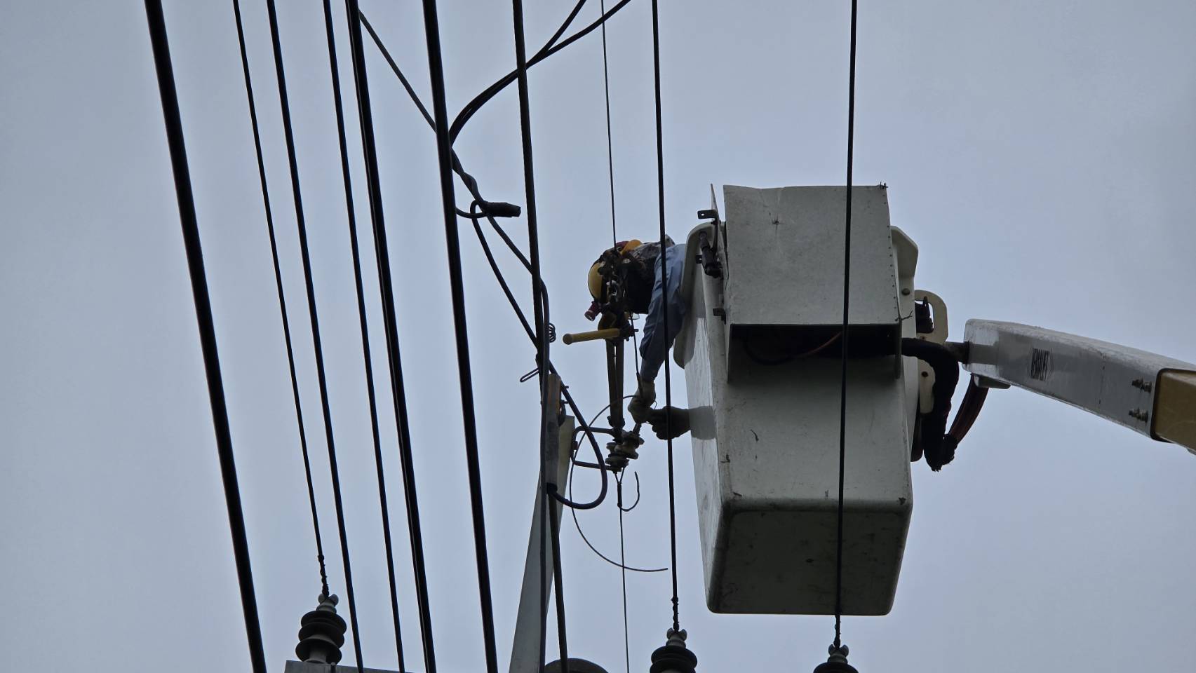▲因強陣風造成架空地線脫落碰觸高壓線,造成停電,台電工程人員頂著強風搶修。(台電提供)