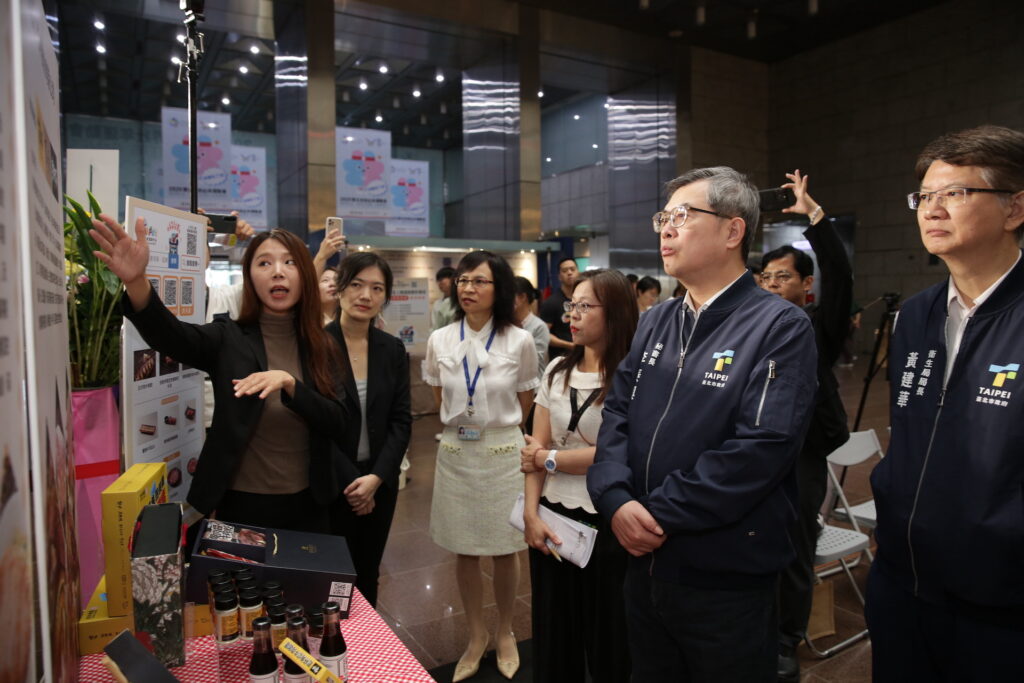 上市上櫃食品業者在現場向臺北市政府秘書長李泰興（右二）臺北市衛生局黃建華（右一）介紹產品。