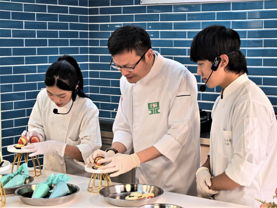 圖/餐飲科三年級鄭竹妘同學(左)教教育局長張明文製作馬卡龍。(新北市政府教育局提供)