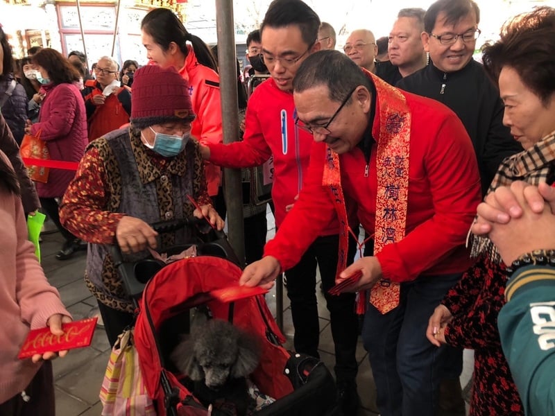 新北市長侯友宜（前右2）29日初一展開拜廟行程，陸續前往板橋慈惠宮、接雲寺等廟宇參香及發放紅包，民眾排隊領取紅包。新北市政府提供