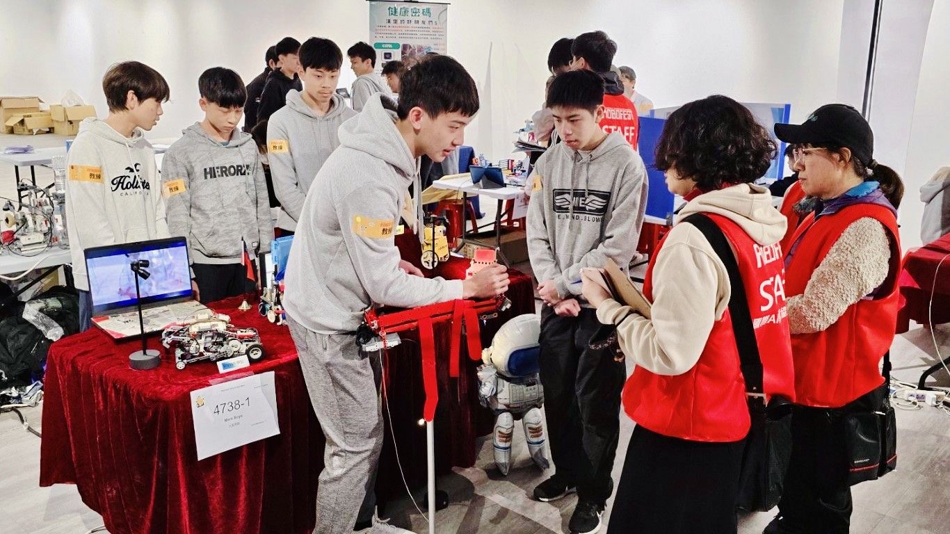 競賽評審時刻,兩位學生站在桌前,靠近兩位穿紅背心的評審。左為吳泓寰,右為徐翌恩。(圖/記者林照東翻攝)