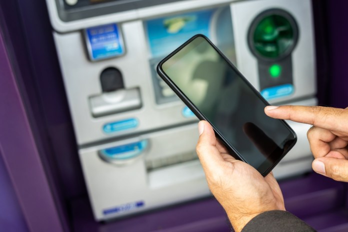 young businessman standing front atm machine using smartphone withdraw money without atm credit card he ut pin code into smartphone take money