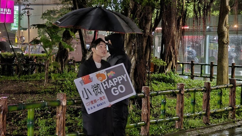 中配「小微」因發布影片涉鼓吹武統言論,遭移民署廢止居留許可,限期昨(31日)前離境,網紅八炯(舉牌者)晚間特地到其住處前舉牌送行。 中央社