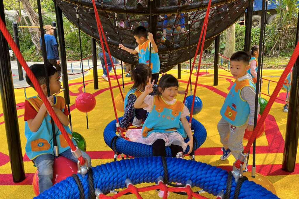 ▲幼兒園孩童在鍬形蟲攀爬架下鞦韆，提升小朋友平衡能力。（土城區公所提供）