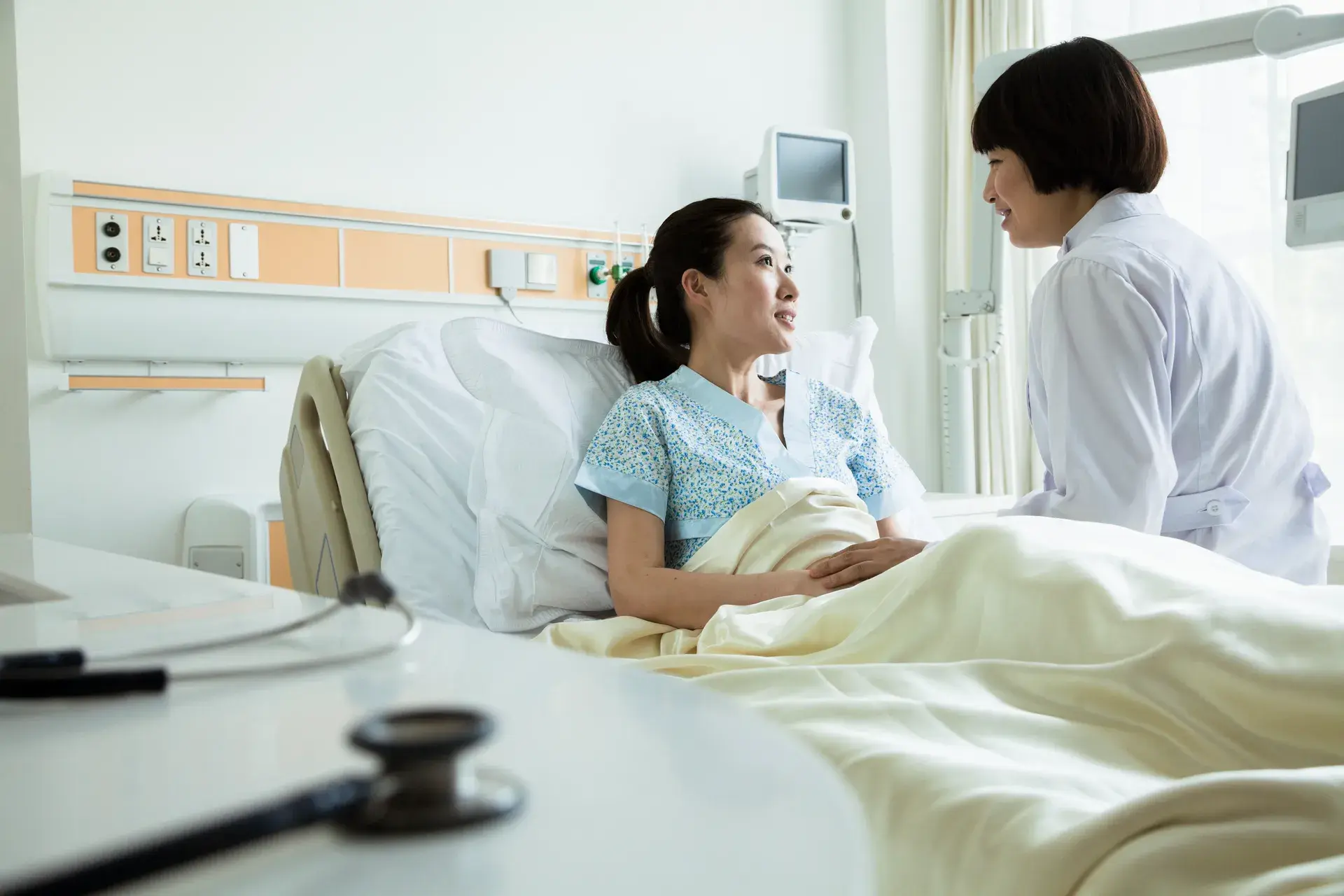 2025安達產險旅平險文章 Female Doctor Sitting On Hospital Bed And Discussing With Young Female Patient