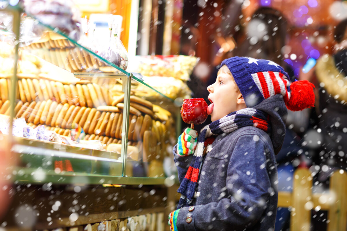 Happy Child Eating On Apple Covered With Red Sugar On Christmas Market