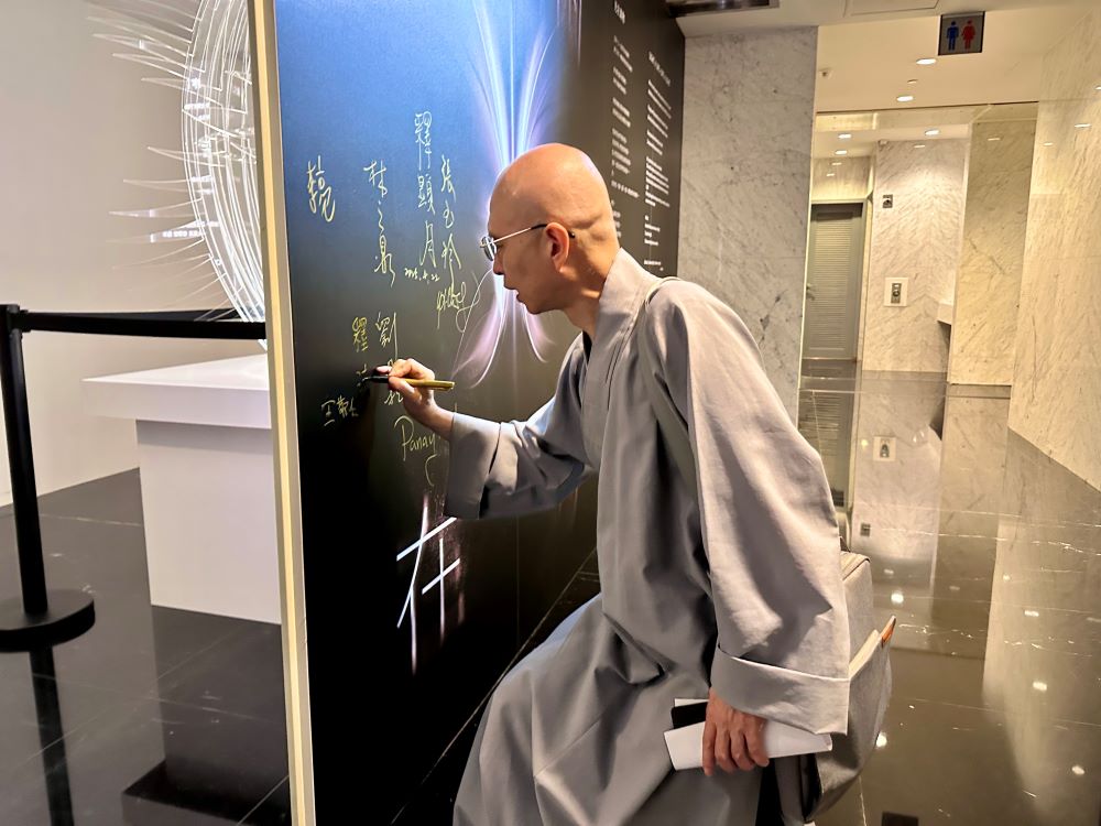 《圖說》法源法師在「光在萬物」特展展板上簽名。〈宗博館提供〉