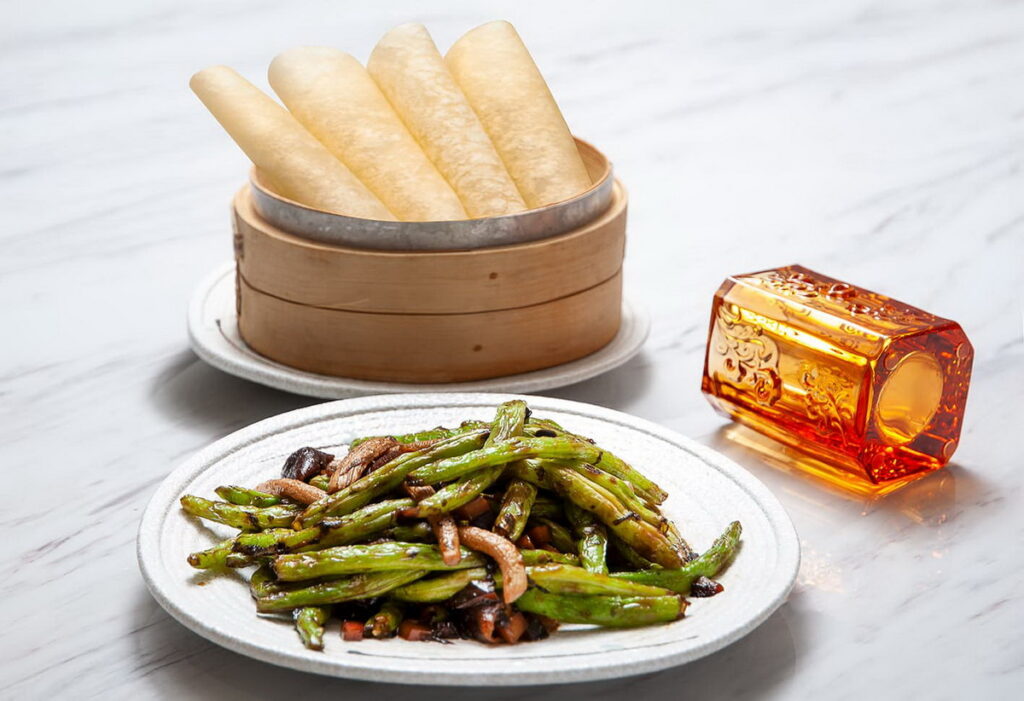 「欖菜松柳煸四季豆」(420元),經典粵式小炒的創新詮釋,主廚加入北方吃法搭配餅皮包卷,提升層次。四季豆煸至乾香爽口,拌以鹹鮮欖菜與菇類快炒,素食也能鮮香誘人,清爽富口感。圖 / 台北凱撒大飯店提供